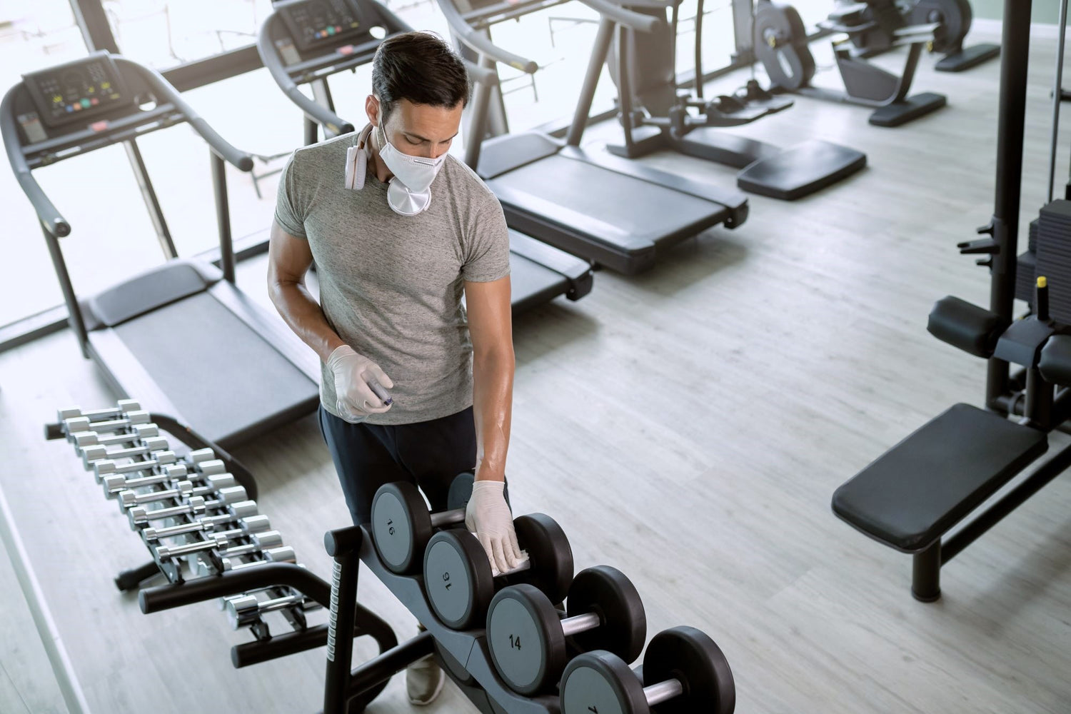 Man using commercial cleaning products to clean dumbbells in a commercial gym