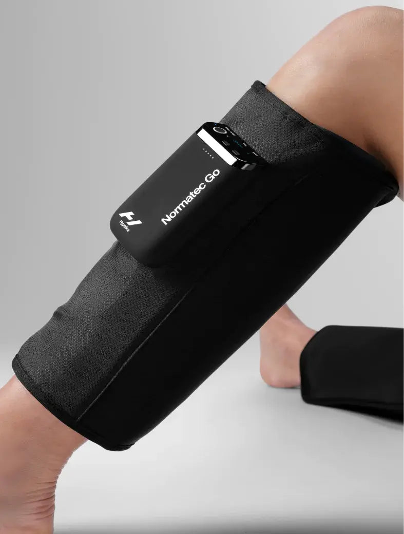 Person using Normatec Go muscle recovery sleeve with chargers